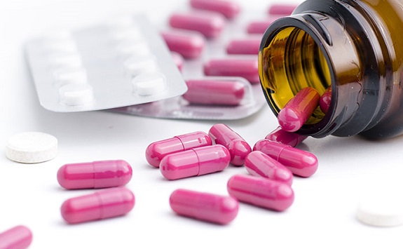 Bright pink capsules and white pills in a blister pack and spilling out of a brown bottle onto a white surface 